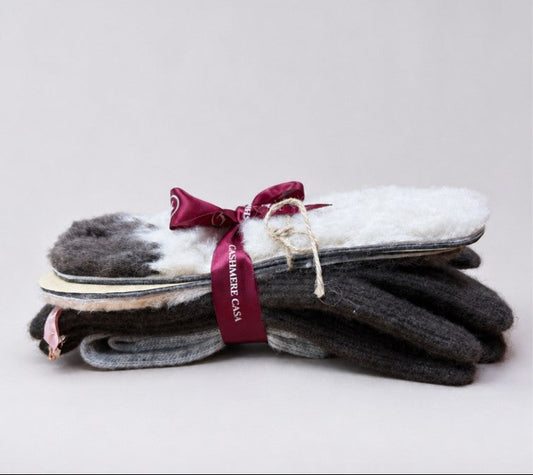 A stack of knit gloves in dark gray, black, and white, tied with a burgundy ribbon that reads 'CARMEN CARR', on a light gray background.