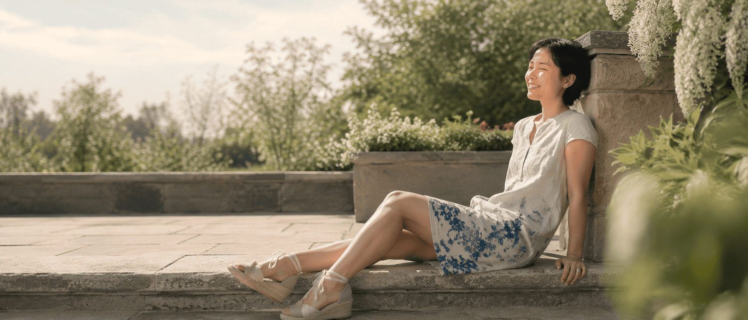 Woman wearing a light linen dress relaxing in a sunny garden